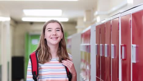 Portrait-Of-Female-High-School-Student-Walking-Down-Corridor-And-Smiling-At-Camera