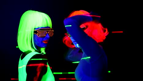 Women-with-laser,-UV-face-paint,-wig,-glowing-glasses,-glowing-clothing-dancing-together-fast-in-front-of-camera,-Half-body-shot.-Caucasian-and-asian-woman.-.