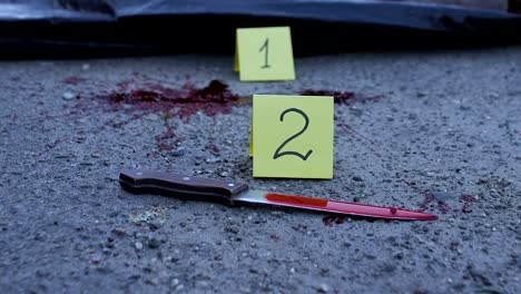 Group-of-forensic-experts-working-at-murder-site,-bloody-knife-lying-on-road