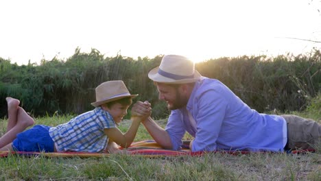 Vater-und-Sohn-spielen-zusammen-im-Armdrücken-und-Spaß-liegen-auf-Karomuster-in-ländlichen