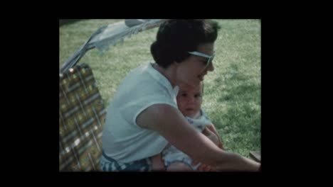 1960-Mom-Feeds-Baby-draußen-sitzen-auf-Liegestuhl