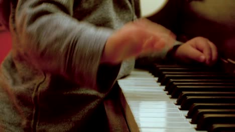 Caucasian-Toddler-Boy,-Sitting-at-a-Piano-with-Him-Mom,-Plays-on-the-Piano-with-a-decorated-Christmas-Tree-Behind-Them