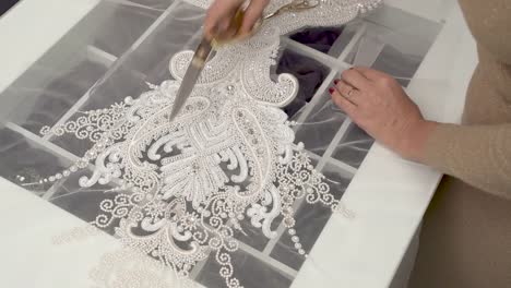 A-top-view-of-a-designer-cutting-out-the-sequined-and-beaded-lace-with-big-scissors-and-then-with-smaller-scissors