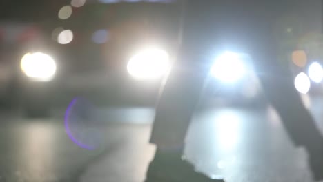 Unscharfe-abstrakte-Fußgänger-überqueren-der-Straße-in-der-Nacht-bei-120fps-slow-Motion.-Lens-Flares-von-Autos-im-Hintergrund-mit-Menschenmenge-im-Vordergrund