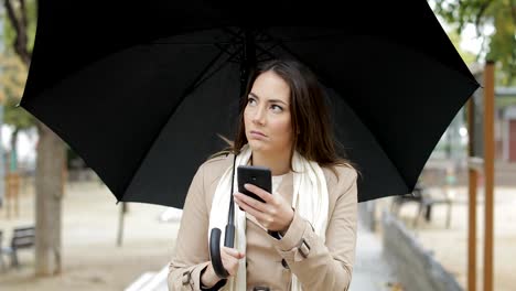 Frustrated-woman-checking-weather-app-under-the-rain