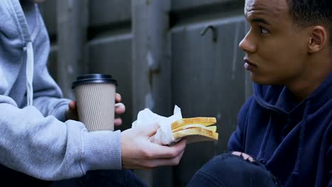 Kind-boy-sharing-tasty-sandwich-and-warm-coffee-with-gamin,-human-compassion