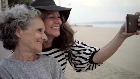 Adult-daughter-grimacing-and-taking-selfie-with-senior-mother