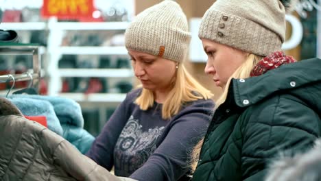 Attractive-woman-and-her-daughter-are-choosing-a-new-down-jacket-in-a-clothing-store