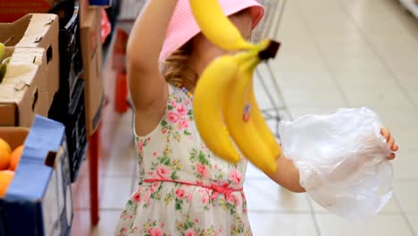 Kindermädchen-im-Laden-wählt-Obstbananen.-Supermarkt-und-Einkaufswagen.