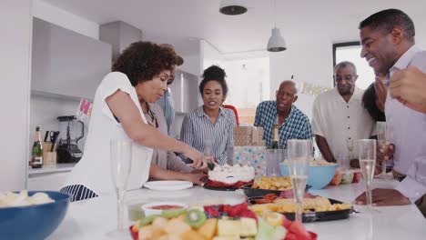 La-familia-negra-de-tres-generaciones-se-mantiene-alrededor-de-una-mesa-mientras-la-madre-corta-el-pastel-en-la-fiesta-de-cumpleaños