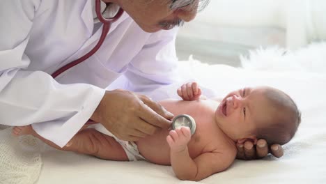 4K-Video-Selective-focus-medium-shot-of-male-doctor-examining--newborn-baby-girl-laying-down-on-white-bed-and-crying-by-use-stethoscope-listening-to-heartbeat