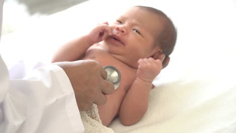 4K-Video-Selective-focus-close-up-shot-of-male-doctor-examining--newborn-baby-girl-laying-down-on-white-bed-and-crying-by-use-stethoscope-listening-to-heartbeat