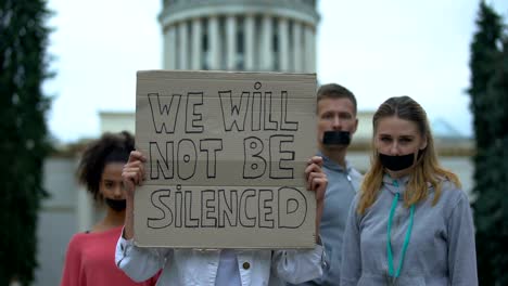 Young-people-with-taped-mouth-showing-banner-against-concealment-of-crime,-abuse