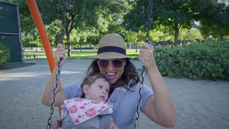 Woman-swinging-on-a-swing-with-baby-on-carrier-at-playground