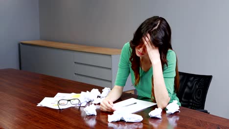 Frustrated-female-executive-sitting-with-crumpled-papers-balls