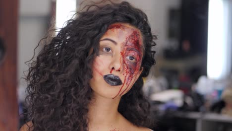 Beängstigend-Porträt-des-jungen-Mädchens-mit-Halloween-Blut-Make-up.-Schöne-Latin-Frau-mit-lockigem-Haar-Blick-in-Spiegelbild-in-der-Umkleidekabine.-Vorbereitung-für-die-Feier.-Slow-motion