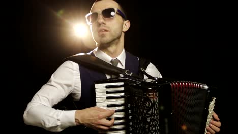 A-fashionable-musician-in-a-white-shirt-plays-the-accordion-in-the-studio-on-a-black-background.