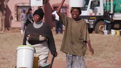 Zwei-afrikanische-Frau-Wasser-aus-Tankfahrzeugen-zu-sammeln-und-zu-Fuß-zurück-zu-ihren-Häusern