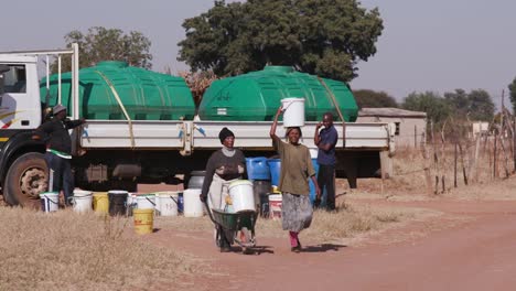 Zwei-afrikanische-Frau-Wasser-aus-Tankfahrzeugen-zu-sammeln-und-zu-Fuß-zurück-zu-ihren-Häusern