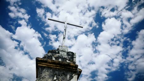 Time-lapse-of-the-clouds-moving-by-an-old-cross-against-a-blue-sky---color-grade