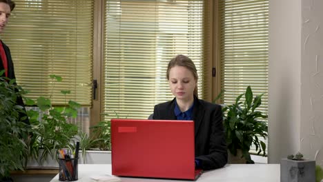 Young-guy-in-suit-flirting-with-girl-in-office,-doing-shoulder-massage,-girl-working-on-computer,-red-laptop.-60-fps