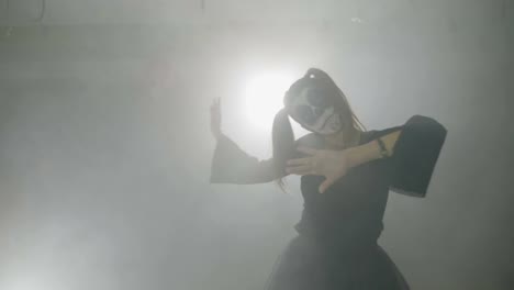 Young-female-teenager-dressed-as-a-sinister-doll-exercising-her-zombie-dancing-moves-in-fog-for-halloween-night-at-club