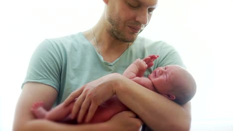 A-newborn-baby-cries-in-the-arms-of-his-father.-The-young-man-calms-the-child,-shakes-him-from-side-to-side,-affectionately-talking-with-him.-Father's-Day