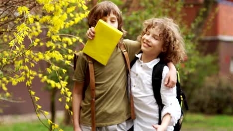 Zwei-jungen-umarmen-und-Blick-auf-die-Kamera.-Schulfreunde-lachen.-Kinder-haben-Schultaschen-hinter-ihnen.-Zurück-zur-Schule.-Tag-des-Kindes