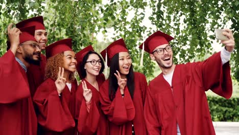 Lenta-de-alegres-estudiantes-graduados-selfie-con-smartphone,-jóvenes-están-posando,-mostrando-gestos-con-las-manos,-riendo-y-haciendo-muecas.