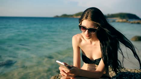 Beautiful-woman-sms-texting-using-app-on-smart-phone-at-beach-sunset-during-vacation