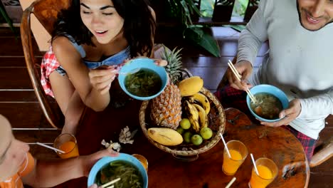 People-Eating-Delicious-Noodles-Soup-Asian-Food,-Friends-Group-Feed-Each-Other-Sit-At-Table-Top-Angle-View