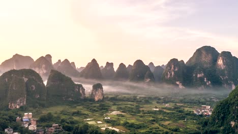 Breathtaking-aerial-establishing-shot-over-beautiful-limestone-karst-mountain-scenery,-covered-with-haze-at-sunset-in,Yangshuo-County,China.Mountain-landscape-top-view