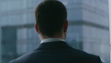 Close-up-Shot-of-the-Thoughtful-Businessman-in-a-Suit-Standing-in-His-Office-and-Contemplating-Next-Big-Business-Deal,-Looking-out-of-the-Window.-Big-City-Business-District-Panoramic-Window-View.