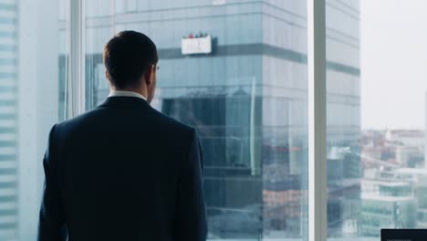 Following-Shot-of-the-Confident-Businessman-in-a-Suit-Walking-Through-His-Office-and-Looking-out-of-the-Window-Thoughtfully.-Stylish-Modern-Business-Office-with-Personal-Computer-and-Big-City-View.