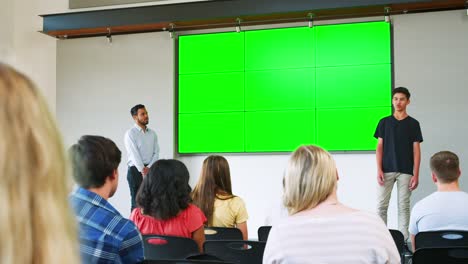 Male-Student-Giving-Presentation-To-High-School-Class-In-Front-Of-Screen