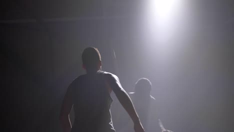 Two-basketball-players-shadow-playing-one-on-one-indoors-in-room-with-smoke-and-floodlit