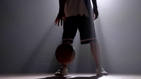 Jugador-de-un-baloncesto-goteo-bola-en-habitación-oscura-niebla-con-proyector