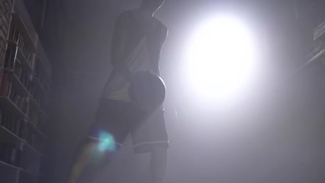 One-basketball-player-silhouette-playing-with-ball-in-misty-dark-room-with-floodlight