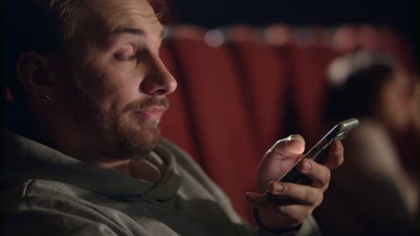 Hombre-enorme-con-smartphone-en-el-cine.-Joven-viendo-película-aburrida