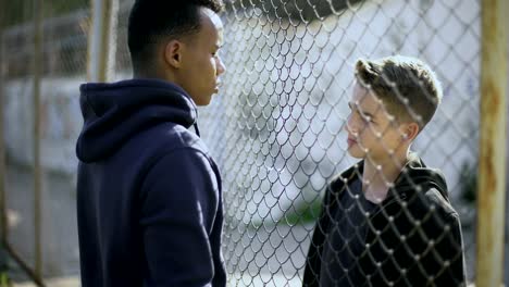 Two-boys-of-different-nationalities-talking,-rich-and-poor-separated-by-fence