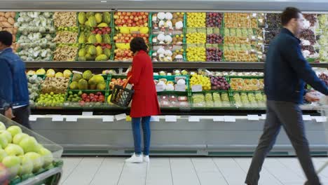 En-el-supermercado:-mujer-elige-producen-de-frutas-orgánicas-en-fresco-de-la-sección-de-la-tienda.-Ella-recoge-melón-y-pone-les-en-su-cesta-de-la-compra.-Vista-trasera-del-tiro.