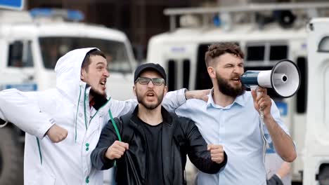 Three-football-feller-on-background-of-police-car.-Boys-shout-into-a-megaphone.