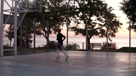 Handhelded-imágenes-de-joven-en-pantalones-cortos-y-calcetines-de-golf-blanco-hace-un-tiro-a-la-canasta-de-baloncesto.-Árboles-al-aire-libre,-en-el-fondo.-Al-atardecer-de-mañana