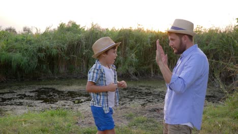 padre-enseñando-a-hijo-boxeo-en-naturaleza,-el-niño-pega-en-las-manos-de-papá-en-puesta-de-sol-de-fondo