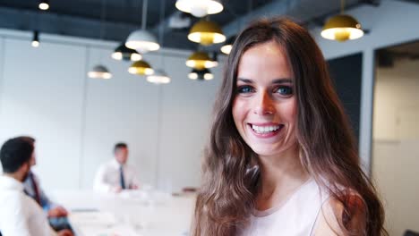 Portrait-Of-Businesswoman-In-Modern-Boardroom-With-Colleagues-Meeting-Around-Table-In-Background-Shot-In-Slow-Motion