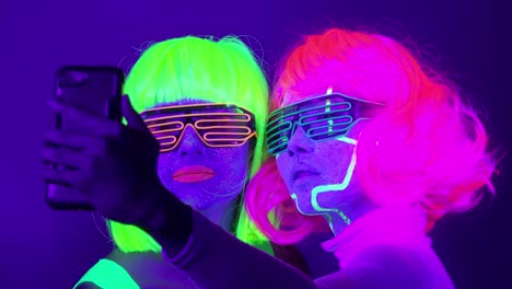 Lento-motin-de-hermosas-mujeres-sexy-con-maquillaje-fluorescente-y-ropa-tomar-foto-selfie-en-luz-de-neón.-Club-nocturno,-concepto-del-partido.