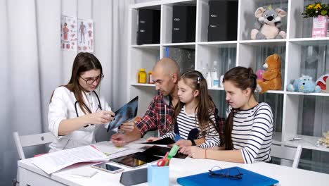 Female-doctor-talking-with-the-father-of-two-daughters,-and-shows-him-x-ray.-youngest-daughter.