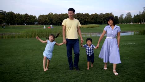 Freudige-asiatischen-Familie-zu-Fuß-halten-Hände-im-park