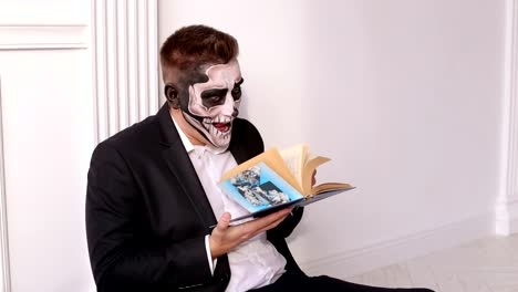 Un-hombre-con-un-maquillaje-terrible-en-forma-de-un-cráneo-sostiene-un-libro-en-sus-manos.