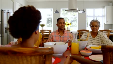 Vista-frontal-de-la-familia-de-generación-negro-multi-orar-juntos-en-mesa-de-comedor-en-hogar-confortable-4k